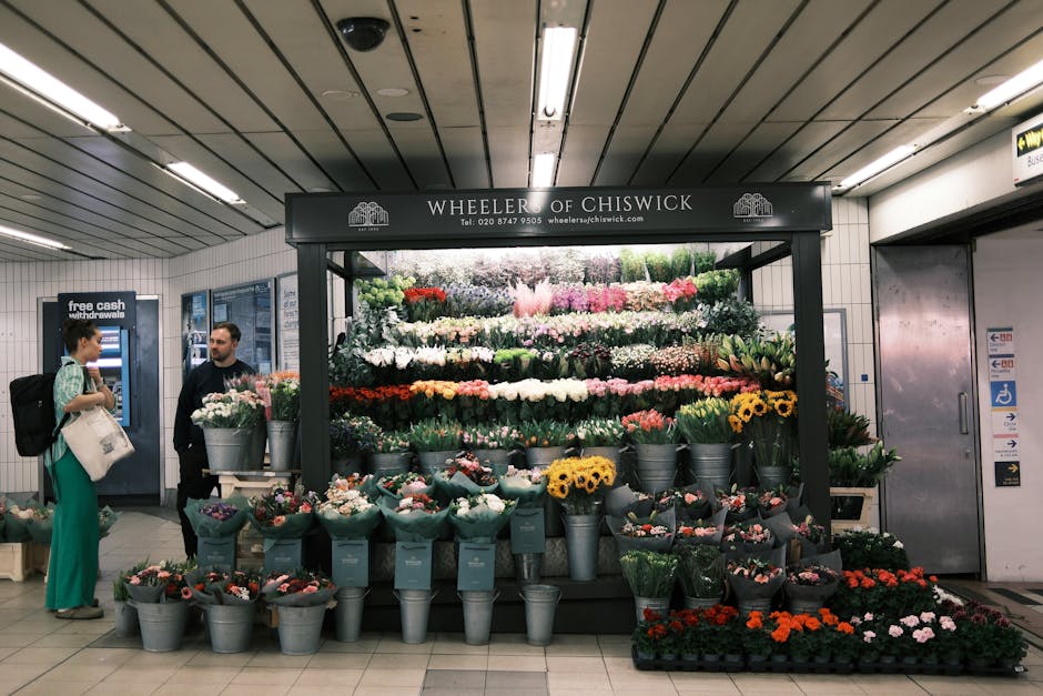 A vibrant floral display at Wheeler of Chiswick in an underground station, featuring a wide arrangement of fresh flowers including white roses, pink carnations, yellow sunflowers, purple and pink tuli